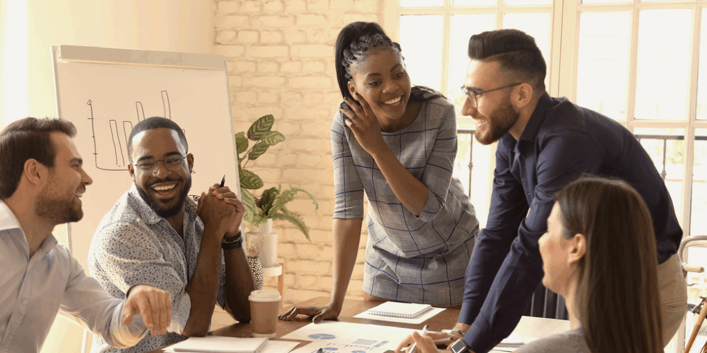 Smiling group of diverse professionals collaborating during a team training session in a modern office, with charts and coffee on the table.